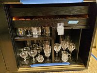 Photo of crystal stemware, drinking glasses, and small glass pitcher displayed on dark shelving unit with 72 pieces total.