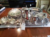 Full view of entire silver plated tea set, serving trays, candy dishes arranged on table.