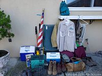 Wide view of the outdoor gear showing coolers, jackets, boots, backpack, chair, and accessories.