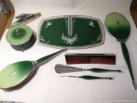 Full set of eight pieces shown including mirror, brush, comb, tray, powder jar, clothes brush, and two manicure tools with gradient green and chrome finish.