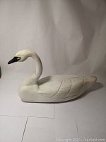 Side view of the entire white wooden swan decoy showing body, wings, neck and head.