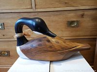 Full side profile of the carved wooden duck decoy on a box against a wood drawer background