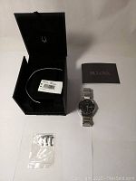 Full lot including original black Bulova box, instruction manual, men's watch, and extra links in plastic bag.