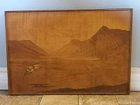 Full view of the rectangular inlaid wood wall hanging showing mountain, water, bird, and grass details in natural wood tones.