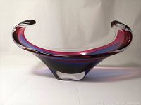 Front view of the elongated art glass sculpture with curled ends, showing blue and red glass layers inside clear glass.