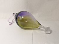 Side view of the teardrop-shaped art glass ornament with purple to yellow color gradient and attached purple ribbon.