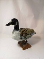 Front angle of the hand painted wooden duck sculpture showing the detailed painting and wood grain, with a visible wood split on the body side.