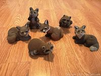 Photo showing six small garden animal statues on floor including raccoons, foxes, bears, all painted in brown and grey tones made of hard plastic.