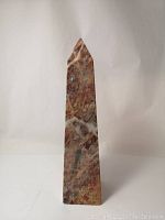 Full front view of the 10-inch tall marble or stone obelisk showcasing its multicolored stone pattern and pointed top.