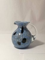 Front-side view showing the bulbous shape with blue and black speckled art glass, clear handle attached to the side, and short spout.