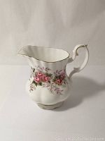 Side angle view of the Royal Albert bone china creamer with pink rose and lavender floral design, gold trim on rim and handle.