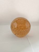 Front view of large amber-colored spherical glass paperweight filled with numerous small bubbles.