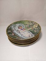 Stack of six decorative plates with visible top plate showing a baby in a lace-trimmed cradle outdoors among pink blossoming branches.