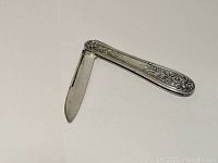 Open pocket knife showing single blade and engraved floral handle detail.