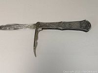 Full view of pocket knife opened showing blade and fold-out tool with etched handle detail.