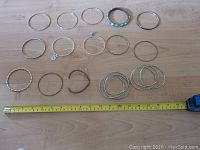 View of all 15 assorted costume jewelry bracelets arranged on a wooden surface next to a measuring tape showing approximately 30 cm scale.