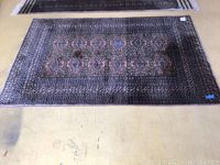Full view of the dark colored antique Bokhara rug with traditional geometric patterns, laid flat on a floor.