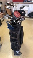 Golf clubs in bag, assortment including irons and drivers with headcovers, clubs numbered 4,6,7,8,9,12 and letters P and D included