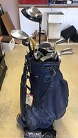 Blue golf bag filled with multiple golf clubs, standing upright.
