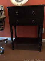 Front view of black vintage wooden side cabinet with two upper drawers and one large bottom drawer, metal ring handles, turned legs.