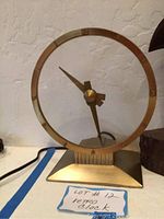 Front view of the vintage metal clock showing the circular open face and gold-tone finish with arrow-shaped hour hand and minute hand.