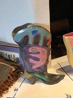 Front and side view of a ceramic boot sculpture with colorful abstract designs.