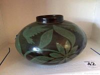 Front and side view of the oval brown ceramic bowl with green leaf decoration placed on a white surface.