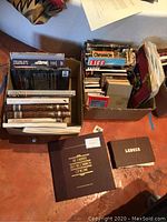 Two boxes of assorted books and vinyl records, including visible book titles and boxed jazz vinyl set.