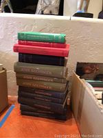Stack of various colored hardbound books including visible titles by John Steinbeck and Ernest Hemingway.