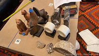 Overall view of four sets of bookends including carved wooden figurines, black stone bookends, white cylindrical stone bookends, and natural geodes.