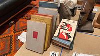 Group photo of multiple vintage books arranged on a patterned rug and wooden floor.