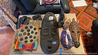 Overview of African art items including two carved masks, plate, necklaces, textile and wooden figurine on a table.