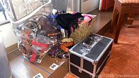 Wicker basket with scarves, bag of belts, and locking makeup case together on the floor.