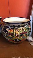 Full side view showing the colorful hand-painted floral and geometric patterns and the pot's shape with handles and rim.