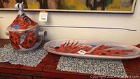 Large covered crock with red floral design sitting next to large oval serving plate with red fish design