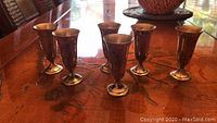 Front view of six sterling silver cordial glasses arranged in a group on a wooden table showing their shape and size.