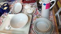 Overview of kitchenware items including platter, pitcher, bowls, baking dish, lidded containers, and butter dish arranged on a patterned cloth