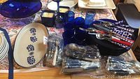 Photo showing cobalt blue glassware, flatware packets, blue dishes, and a blue candle holder on table.