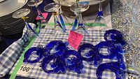 Overview photo showing eight cobalt blue glass napkin rings with floral accents and seven glasses with blue and clear designs.
