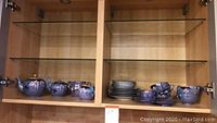 Full shot of tea set on glass shelf including teapot, sugar bowl, creamer, teacups, and saucers arranged
