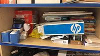 Shelf with multiple boxes of HP and Epson printer cartridges, Epson photo paper, and assorted papers