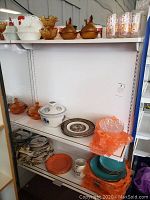 Shelf with amber hen candy dishes, blue and white ceramic lidded dish, glass and stoneware plates, orange glass bowls with crinkled design