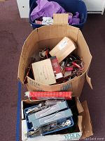 Photo showing large cardboard box filled with assorted kitchen utensils, cutlery boxes, and packaging.