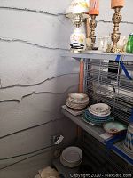 View of brass candle holders, stacked plates on shelving, and bowl