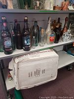 Shelf with vintage beer and liquor bottles including a Coca Cola bottle, an ornate skull-shaped liquor bottle, and apothecary bottle with cork stopper.