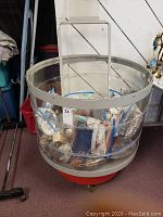 Clear plastic storage barrel on wheels containing assorted items mostly in zip lock bags.