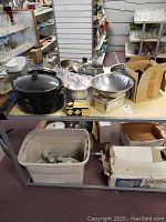 Photo of assorted kitchenware on table including American Way popcorn popper, pots, pans, metal mixing bowls, cookie cutters and more.