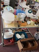 Overview of multiple kitchen items including Corning Ware baking dishes, cupcake carrier, plastic dish set, beverage dispenser, canister, dish rack, foot spa, and bowls on shelving unit