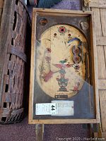 Top-down view of antique pinball machine showing playfield with faded markings and broken glass cover.