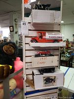 Four model cars displayed on and in boxes, including the Esso Gasoline tanker truck, 1955 Cadillac Eldorado, and others stacked vertically on a shelf.